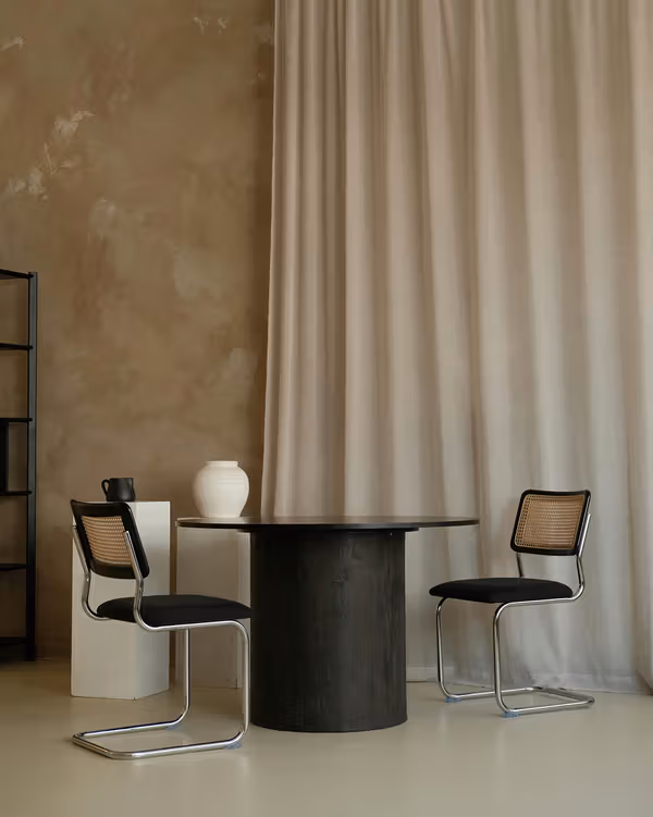 Two cantilever chairs beside a round black table and floor-length curtains.