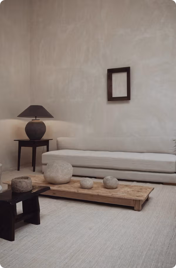 A neutral-toned living room with a low wooden table, stone objects, and a long sofa.