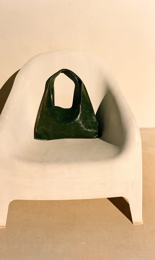 A dark green handbag centered on a rounded cream chair.