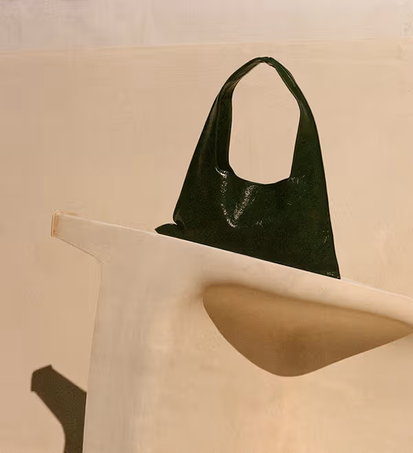 A dark green handbag resting on a pale sculptural chair.