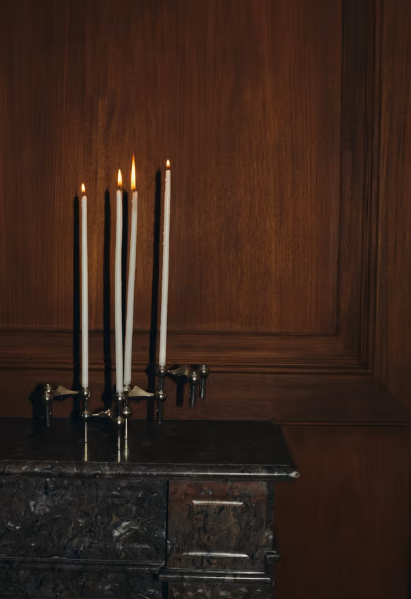 Lit taper candles on a dark cabinet against a wood-paneled wall.